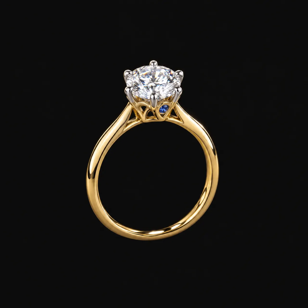 Le solitaire Comtesse sur fond noir : anneau en or jaune, diamant rond, six griffes en or blanc, corbeille d'arceaux et petit saphir bleu